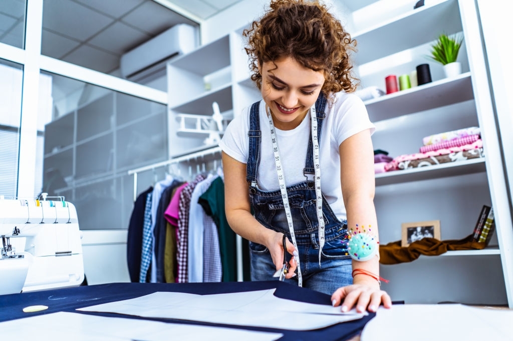 The cute tailor sews a dress on the table